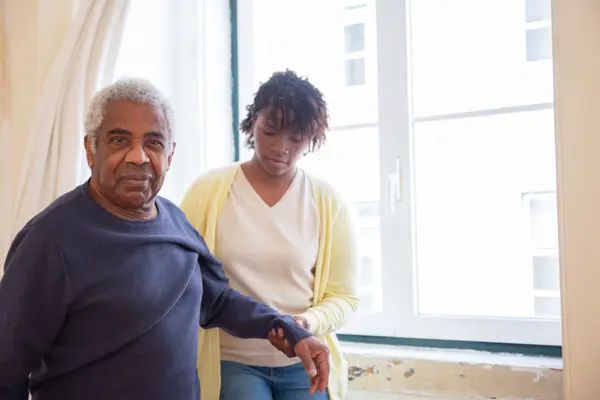 A caregiver standing beside an elderly man at his window