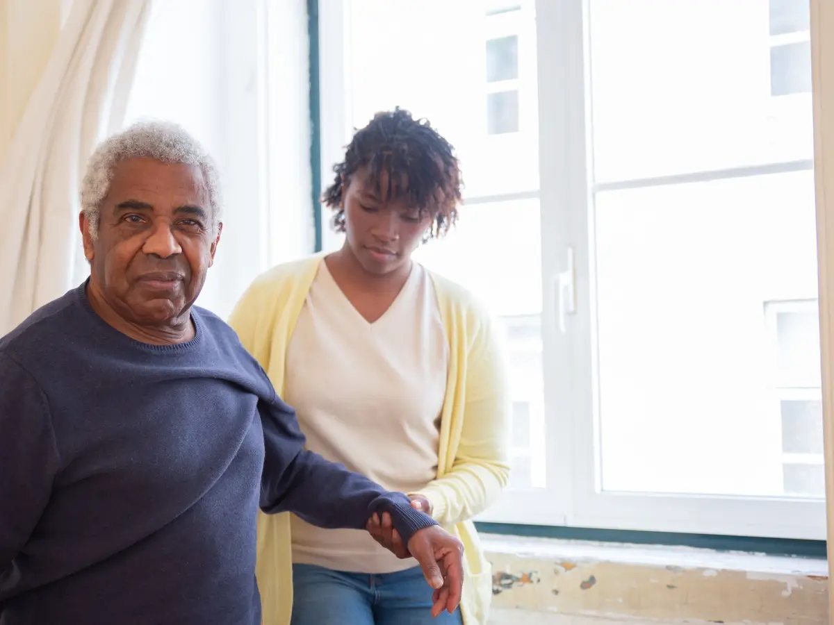 A caregiver standing beside an elderly man at his window