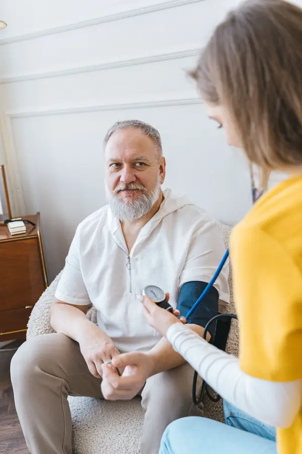 A nurse checking an elderly man’s blood pressure in his living room