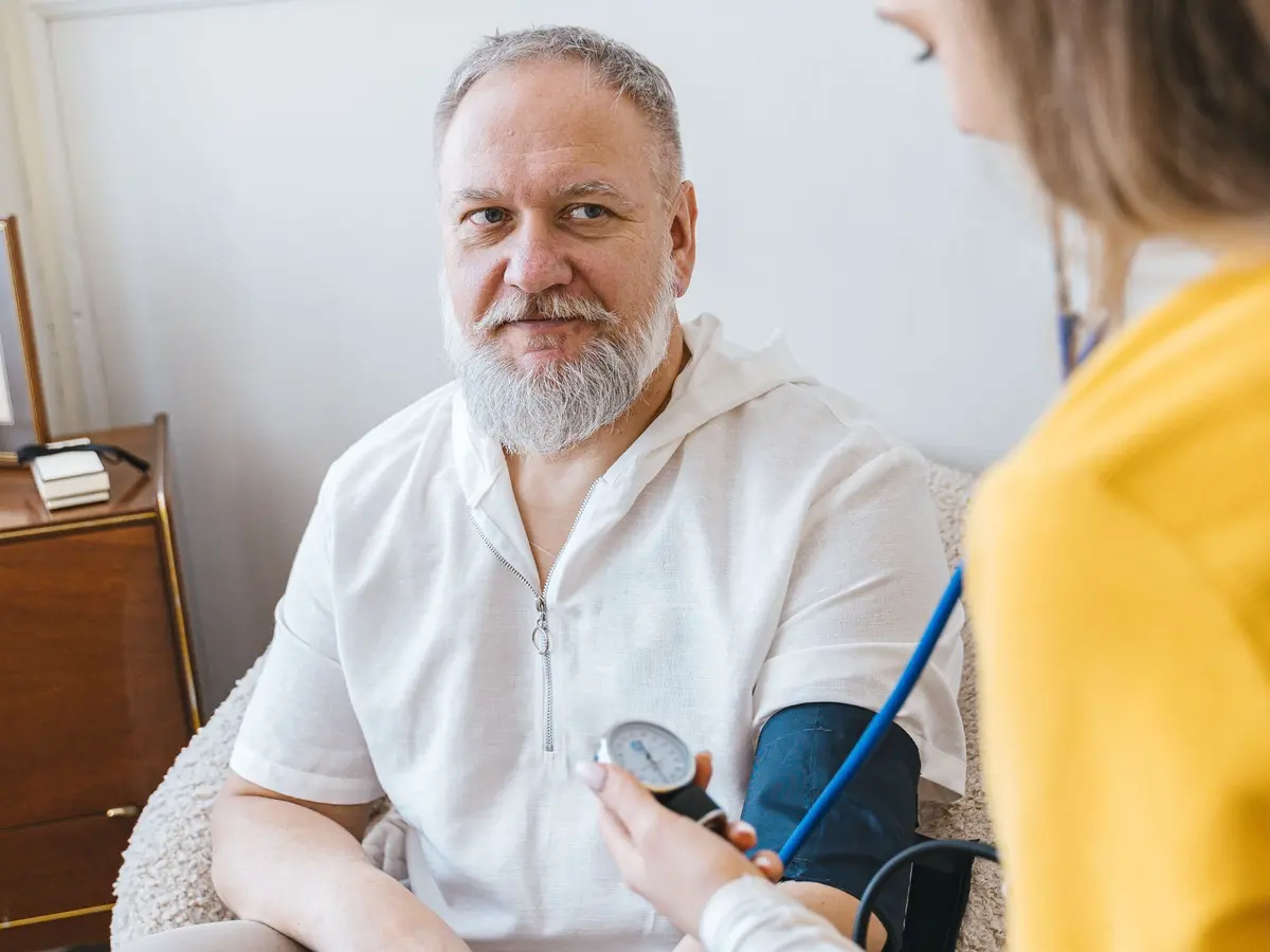 A nurse checking an elderly man’s blood pressure in his living room