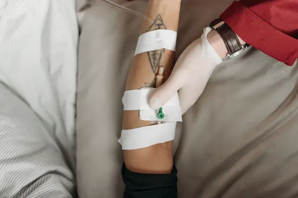 An IV line secured on a patient’s arm while resting in bed at home