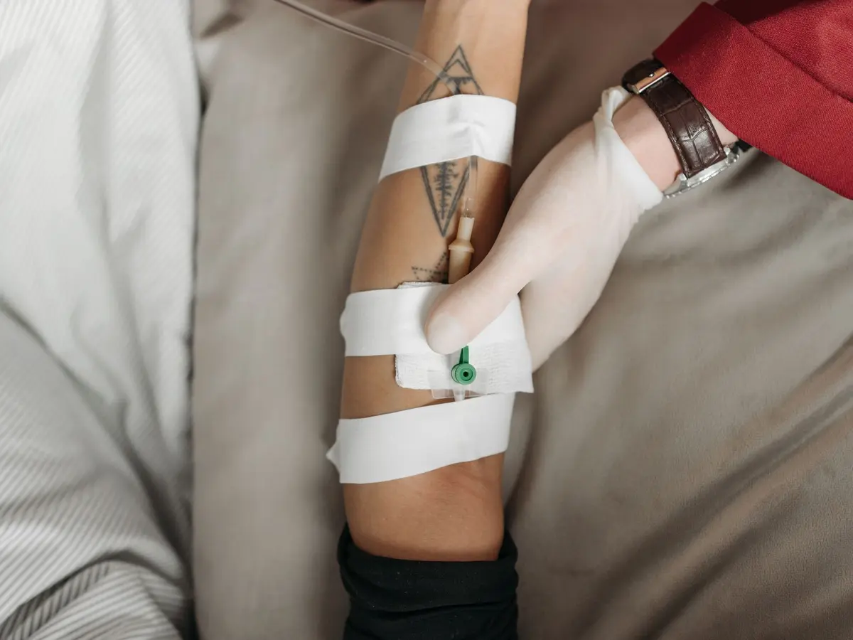 An IV line secured on a patient’s arm while resting in bed at home